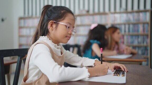 戴眼镜学习的亚洲女学生在教室里用笔记本写笔记正在学习准备考试的女学生小学生在课桌上写字教育知识观
