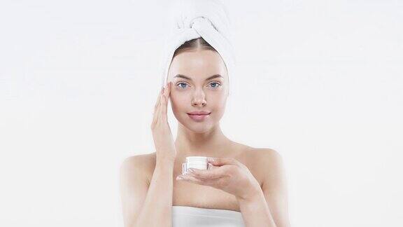 年轻女性用手拿面霜涂在脸上滋润完美的皮肤化妆品广告