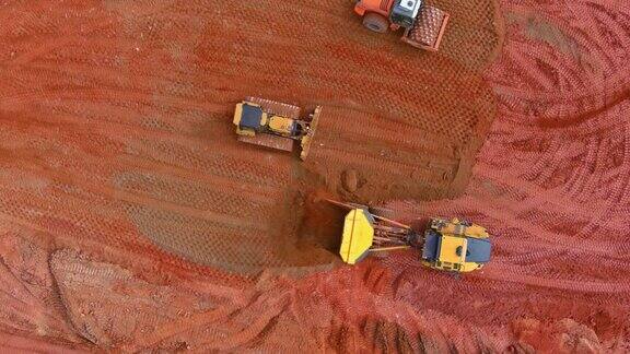 工业履带式挖掘机在工作过程中挖出泥土倒在自卸车上的鸟瞰图