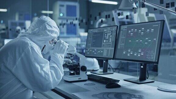 研究工厂洁净室:工程师科学家穿着工作服和手套用显微镜检查主板微处理器组件开发高科技现代电子