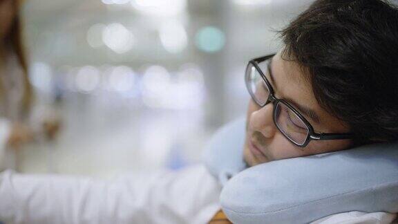 一个疲惫的亚洲商人枕着颈枕在机场候机楼睡觉