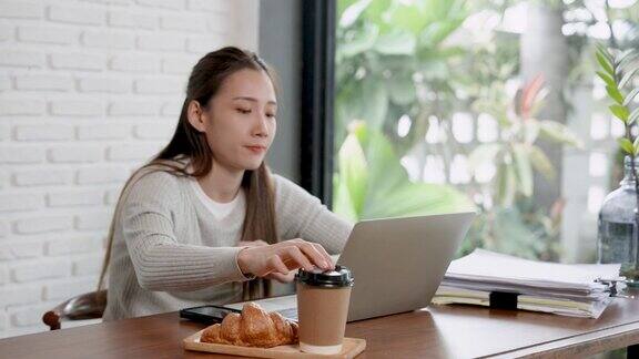漂亮的亚洲女人在晴朗的日子里坐在咖啡馆里带着笔记本电脑的女人在咖啡馆工作改变了工作环境但在假期里工作很累应该休息一下