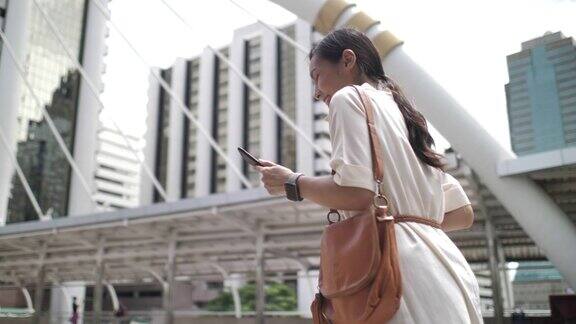 一名亚洲女性正在用智能手机和朋友在线聊天走在办公大楼里