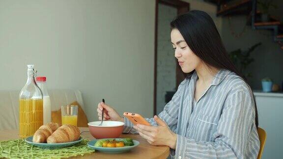 亚洲女性在家厨房吃早餐和使用智能手机的肖像
