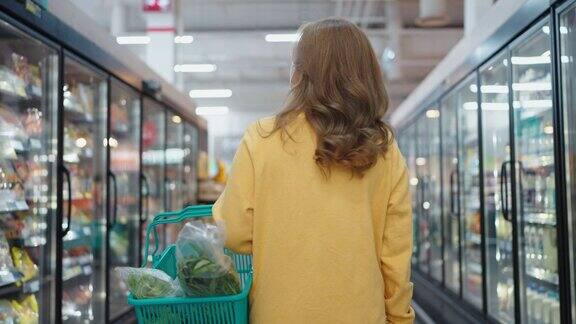 背影的女人走着在超市里拿着篮子购物