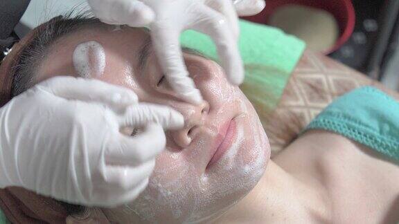 在美容诊所医疗和美容皮肤科预约概念中用泡沫和手清洁亚洲女性的脸