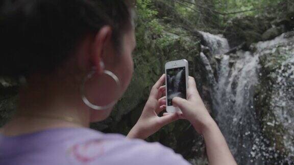 女游客用智能手机拍下森林深处的瀑布