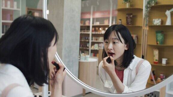 漂亮的亚洲女孩在镜子前尝试新的口红颜色