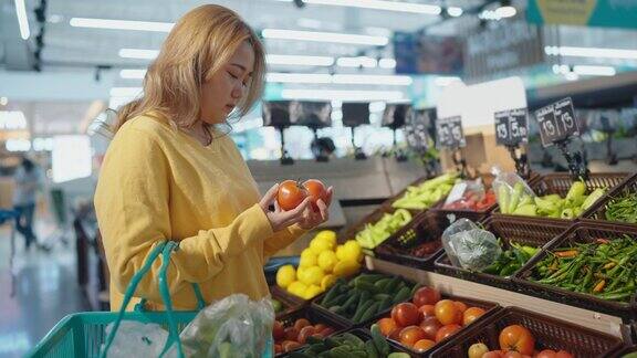 一名妇女在超市的货架上采摘西红柿并把它放在篮子里