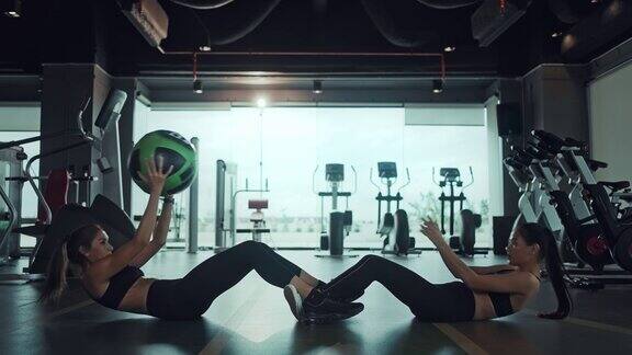两个运动的女人在健身房做仰卧起坐和传球健康的生活方式