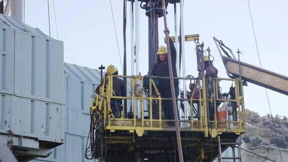 在一个寒冷的冬天的早晨油田工人在石油和天然气钻井平台的一个高高的金属平台上装配钻杆