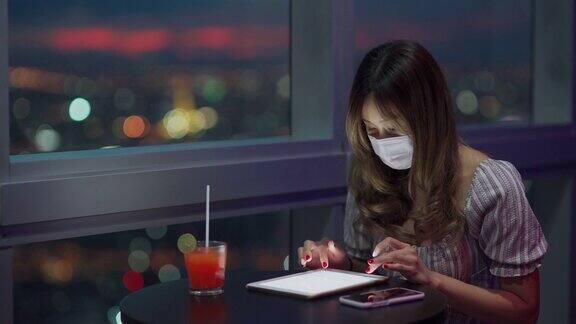 工作到深夜的亚洲女性在家办公时戴着口罩使用平板电脑