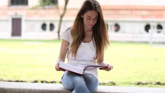 美丽的女大学生在公园的长椅上看书