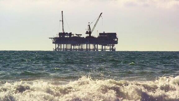 海浪冲刷海岸亨廷顿海滩在南加州与海上石油钻井平台在地平线上在远处的慢动作拍摄