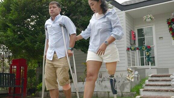 戴着义肢的妇女用拐杖帮助在事故中受伤的丈夫平等观念残疾生活困难