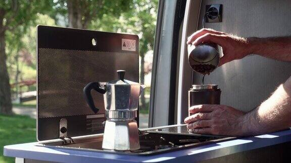 公园里停着一辆露营车一名男子双手将咖啡豆倒入电动研磨机