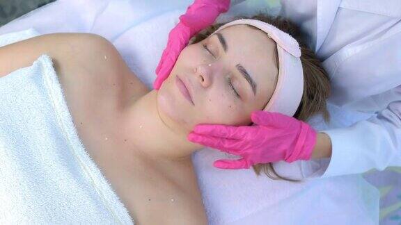 美容师戴着手套在客户女士脸上涂抹护肤霜按摩皮肤