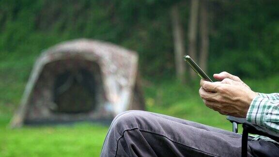 亚洲男子在公园露营度假时使用手机