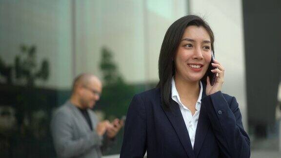 自信的商务人士使用智能手机和应用程序在城市商业大楼进行通信成功的美女在现代办公大楼前使用手机工作的女人