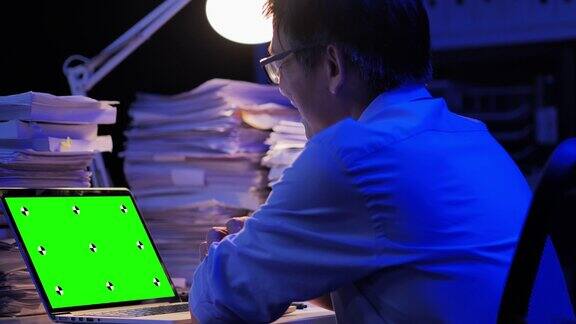 57岁的亚洲高级男子看着绿色屏幕在远程地点通过电脑在家里工作到深夜绿屏新技术概念