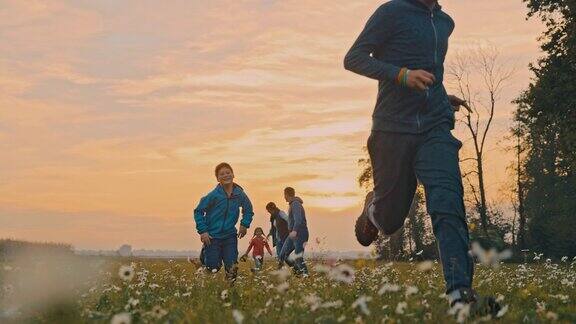 SLOMOYoung家庭在日落时在草地上跑步