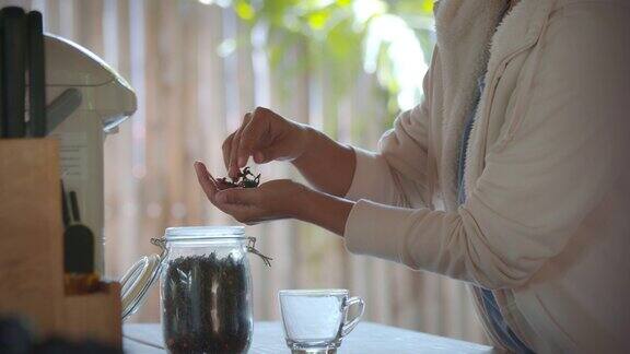 慢镜头拍摄的亚洲妇女采摘干茶叶的手闻到香气的茶在厨房里而在早上的时间在家休息