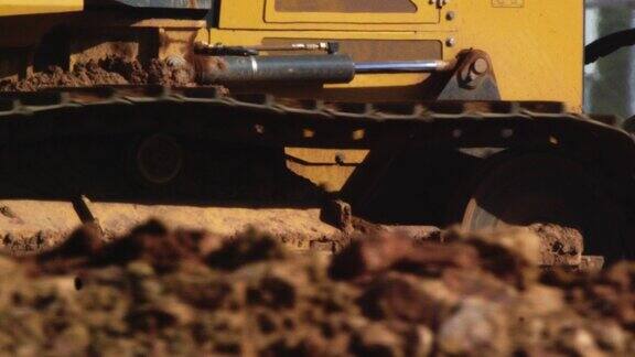 一辆推土机的钢轨在建筑工地的泥土上滚动的侧面视图
