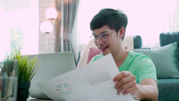 4K一个穿着绿色衬衫的年轻亚洲人的特写通过笔记本电脑解释他的工作一张纸是他的工作有一个微笑的脸和手势