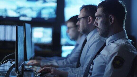 一群安全人员正在一间充满显示屏的黑暗监控室里工作
