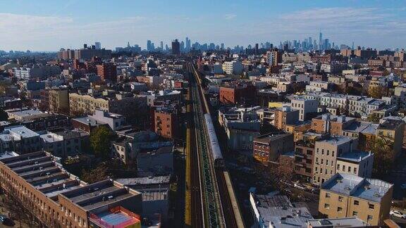 日落时分一辆火车正驶过纽约布鲁克林的住宅区远处曼哈顿的背景无人机视频带着摄像机向前移动跟踪火车