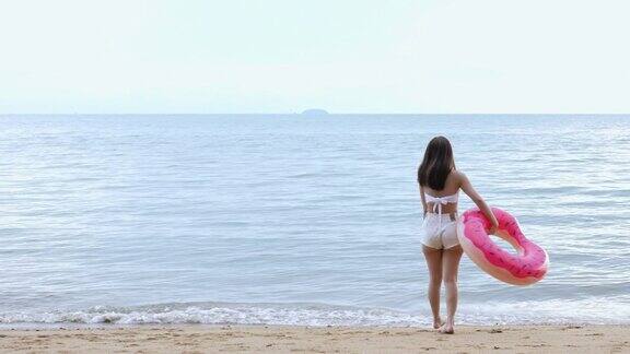 身穿比基尼泳装的年轻亚洲女性戴着橡胶圈在海边海滩漫步热带休息和放松的旅行生活方式快乐的女性自由在暑假的周末时间