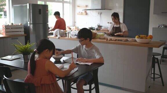 两个孩子在家学习写中国书法而他们的母亲在厨房柜台准备食物