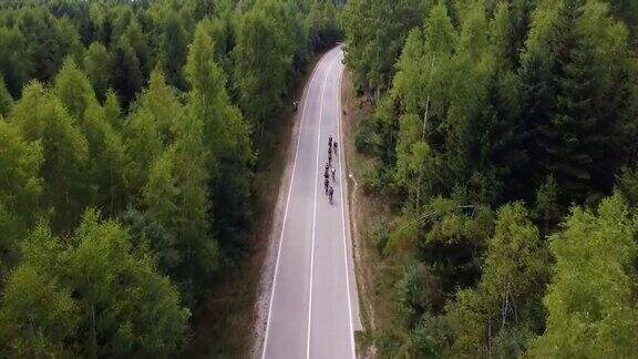 在铁人三项比赛期间一群铁人三项运动员骑自行车在森林包围的道路上的无人机视图