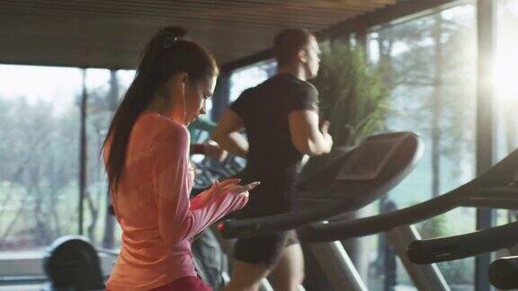 适合运动的白人女孩开始在跑步机上跑步在体育健身房与耳机