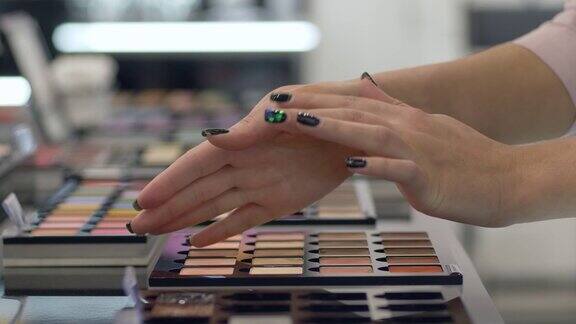 专业化妆客户女孩的手臂从调色板中选择不同颜色的专业化妆眼影并在购物中心随手涂抹化妆品
