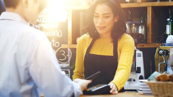 在咖啡馆里一位西班牙美女正在为一位通过非接触式手机向信用卡系统付款的顾客制作外卖咖啡