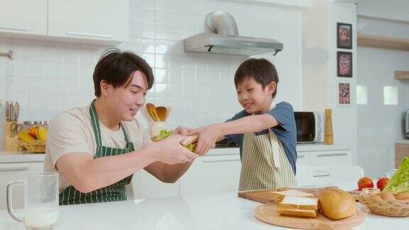 快乐的年轻亚洲父亲和儿子在家里的厨房吃健康的食物