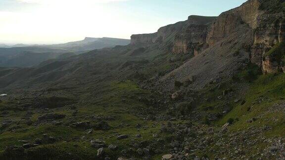 沿着岩石悬崖飞行在山脚下的史诗峭壁的高原在北高加索以4k100mbps的速度飞过布满石头的绿色田野