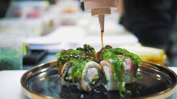 寿司日本的食物烹饪烹饪特写镜头寿司师傅正将酱汁浇在盛在黑色盘子上的新鲜寿司卷上在餐厅服务的艺术亚洲食物