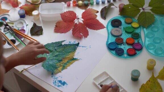 小女孩用水粉在秋天的黄叶上画画孩子们的艺术孩子们的创造力秋天的艺术