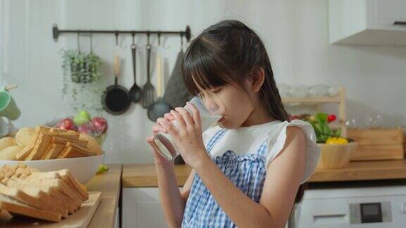 亚洲小孩拿着一杯牛奶在家里的厨房里喝幼小的学龄前女孩或女儿喝牛奶弄乱了牛奶的胡子和嘴唇后在家里的医疗保健