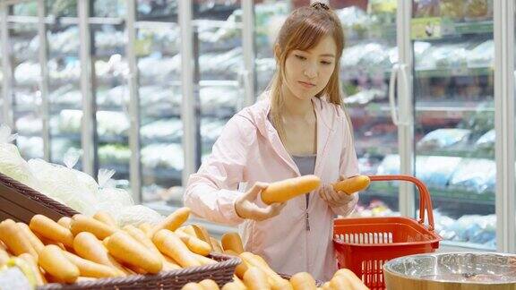 一位亚洲妇女在超市的摊位上挑选胡萝卜
