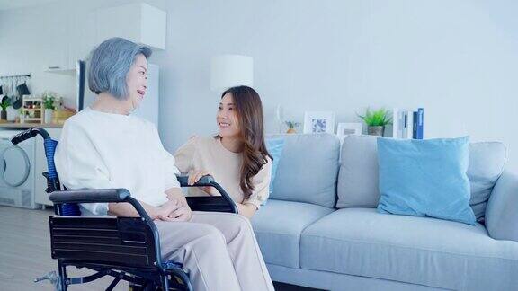 亚洲年轻的女儿在家照顾坐轮椅的残疾老太太美丽的女孩帮助和照顾年迈成熟的残疾母亲病人做物理治疗在客厅在家里