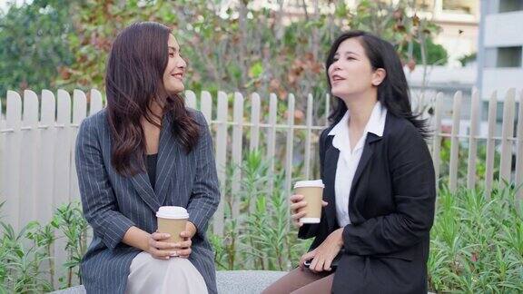 两个亚洲女商人在商业区的公园边喝咖啡边聊天