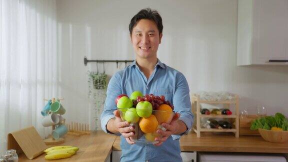 亚洲帅哥的肖像拿着水果碗看着镜头年轻有魅力的男士在空闲时间享受在家吃干净的蔬菜保健饮食与健康食品理念