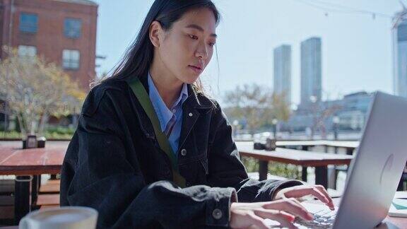 年轻的亚洲女性在户外咖啡馆用笔记本电脑工作