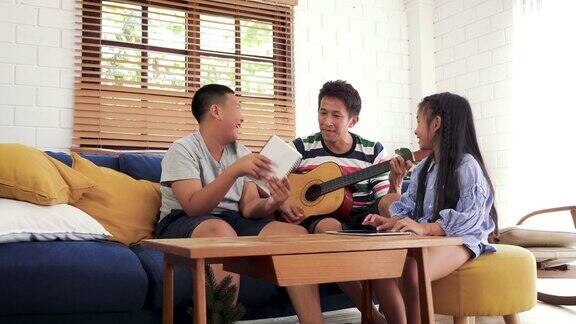 快乐的亚洲家庭喜欢坐在家里客厅的沙发上一起唱歌和弹吉他家人在家里一起放松和消磨时间