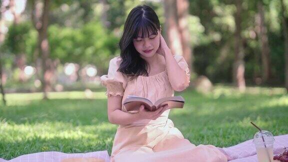 迷人的亚洲年轻女子在阳光明媚的日子里在美丽的绿色花园外野餐和读书在夏日假期放松