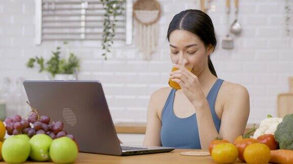美丽的亚洲女人在厨房在家里她在厨房用笔记本电脑喝橙汁保健和饮食