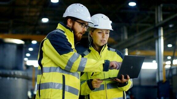 男和女工业工程师在安全帽讨论新项目同时使用笔记本电脑他们会做一些有表现力的手势他们在重工业制造厂工作长针